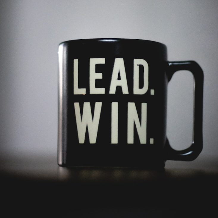Schwarze Tasse mit der Aufschrift "LEAD. WIN." in großen, hellen Buchstaben.